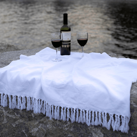 Two wine glasses on top of a white Turkish towel by the lake. 