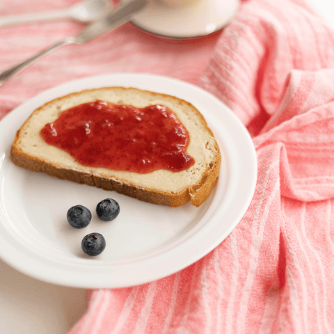 Toast with jam and blueberries served on a plate placed on a red Turkish towel.