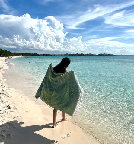 Woman holding a green Turkish towel on a sunny beach near blue water
