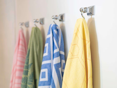 several Turkish towels in pink, green, blue and yellow hang on hooks in the bathroom