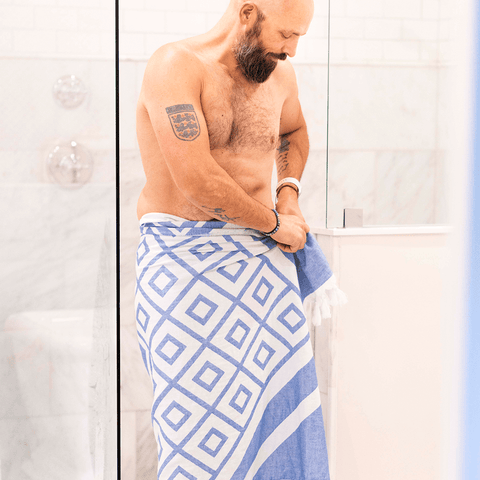 Man coming out of a shower wrapping himself in a blue and white Turkish towel