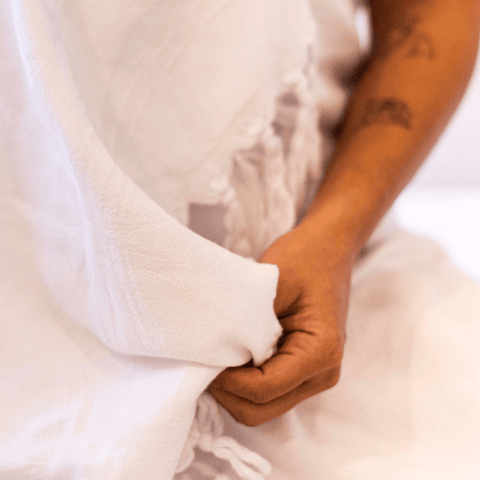 A close up of a white Turkish towel being held by a tattooed arm.