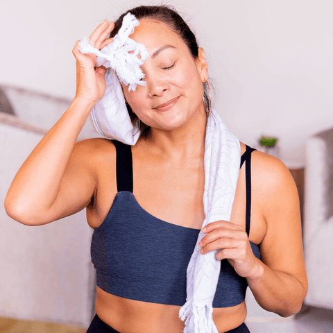 Latina woman in workout clothing dabbling her forehead with a Turkish towel after a workout.