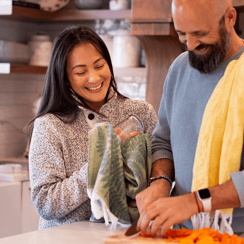Two people, a Latina woman and a man using a yellow Turkish towel as well as a green one to use while cleaning up and cooking.