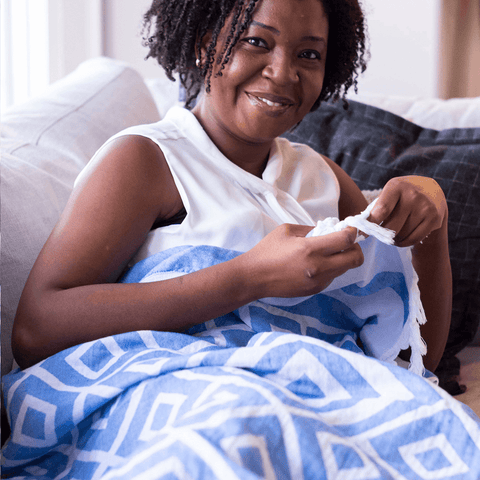 Woman of colour wrapped in a blue patterned Turkish towel on the couch.
