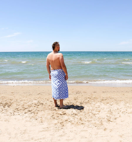 Shirtless man on the beach wearing a blue white Turkish towel around his waist
