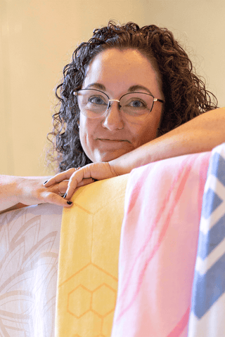 Woman leaning over various colours of Turkish towels. 