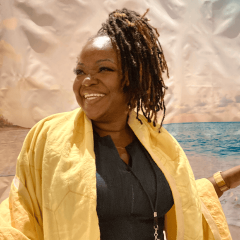 Woman of colour smiling while having a yellow honeycomb Turkish towel draped over her shoulders.