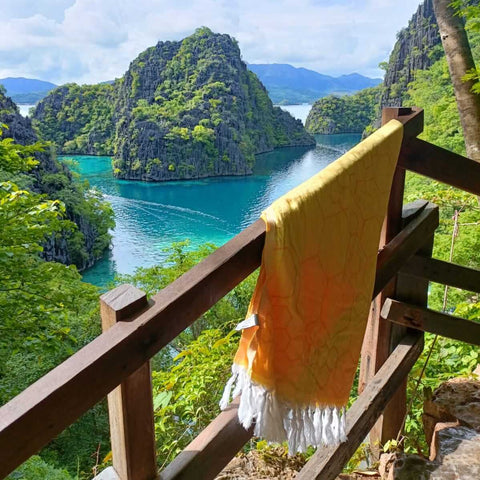 Yellow honeycomb Turkish towel hanging on a wooden railing overlooking water and hills in the Philipines