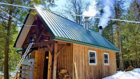 lieu-no3-photo-exterieure-cabane-a-sucre-murs-bois-toit-tole-vert-cheminees-fumee-neige-ciel-bleu-production-sirop-derable