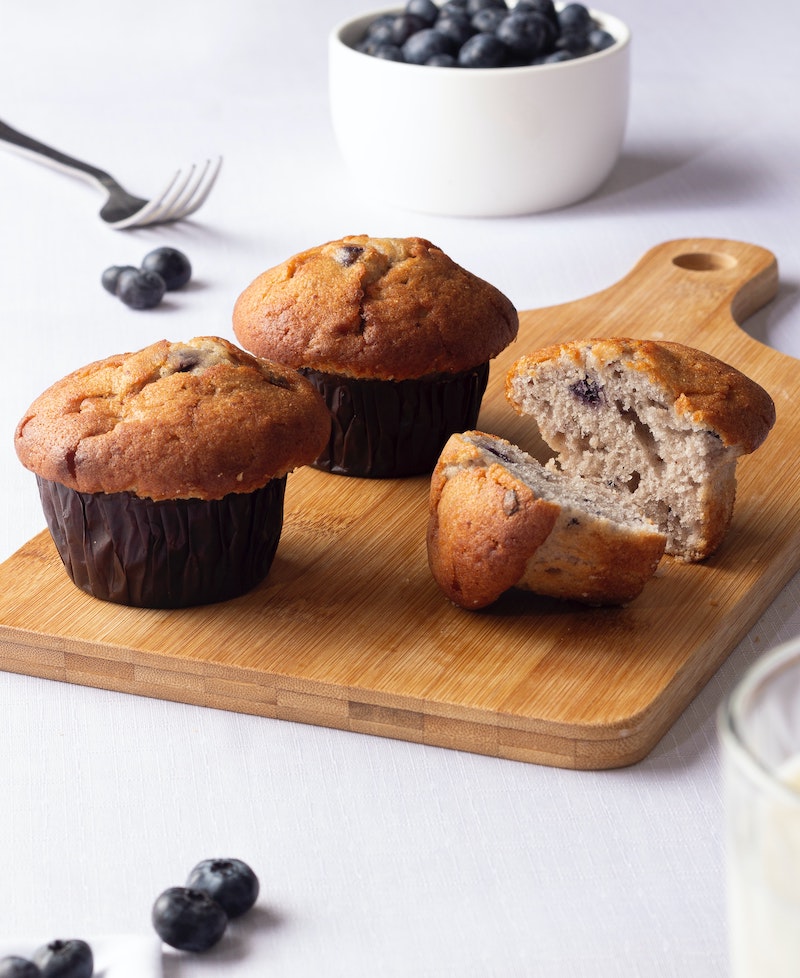 Homemade protein blueberry muffins on a wooden chopping board, with a bowl of blueberries in the background