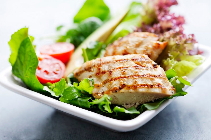 Cooked chicken added to a salad containing tomatoes, lettuce, and avocado