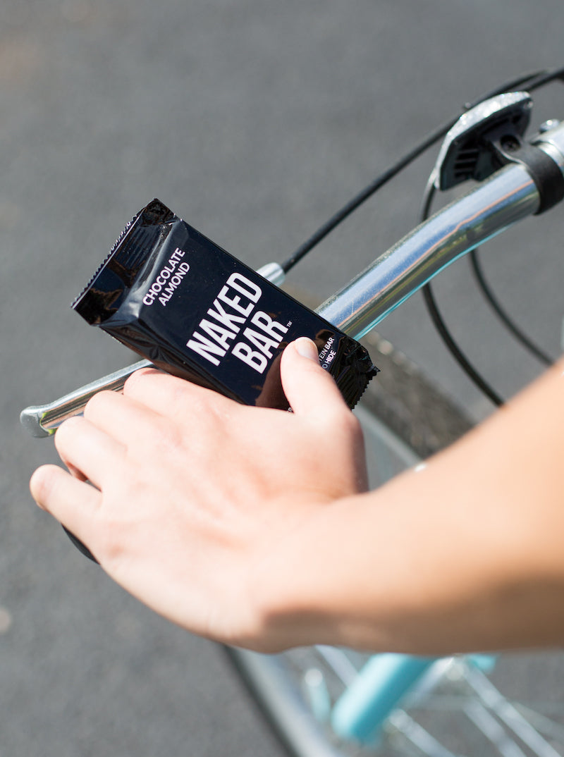 Close up of a bike's handlebars while somebody is holding a Naked Nutrition Naked Bar