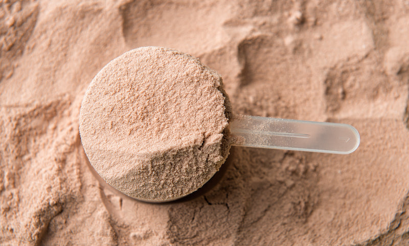 Aerial view of a scoop of chocolate whey protein powder in front of a heap of protein powder