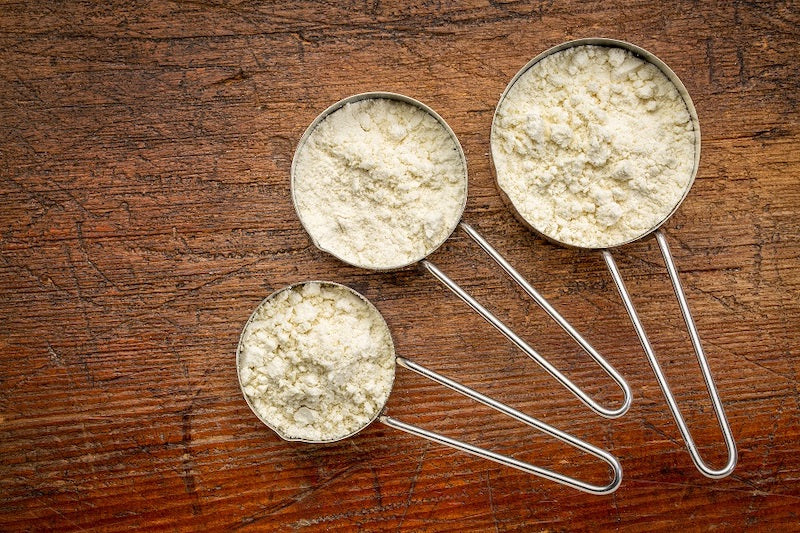 Three different sized metal scoops of protein powder on a wooden surface