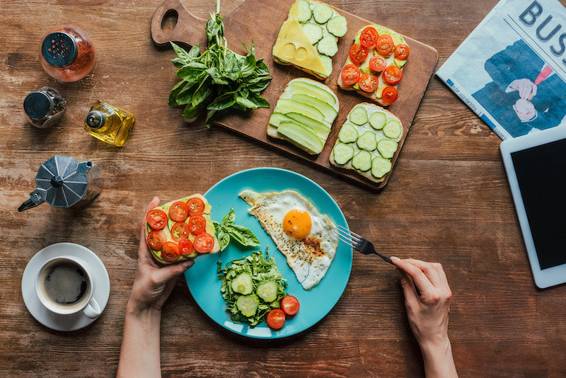 Aerial view of a healthy breakfast spread on a wooden table with a woman's hands in the shot picking up a piece of toast