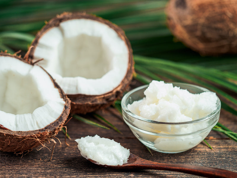 MCT oil in a solid form in a clear glass dish, with two halves of a coconut next to it