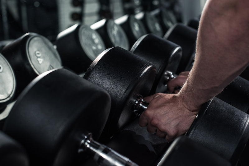 Man picking up dumbbells from a weight rack at a gym