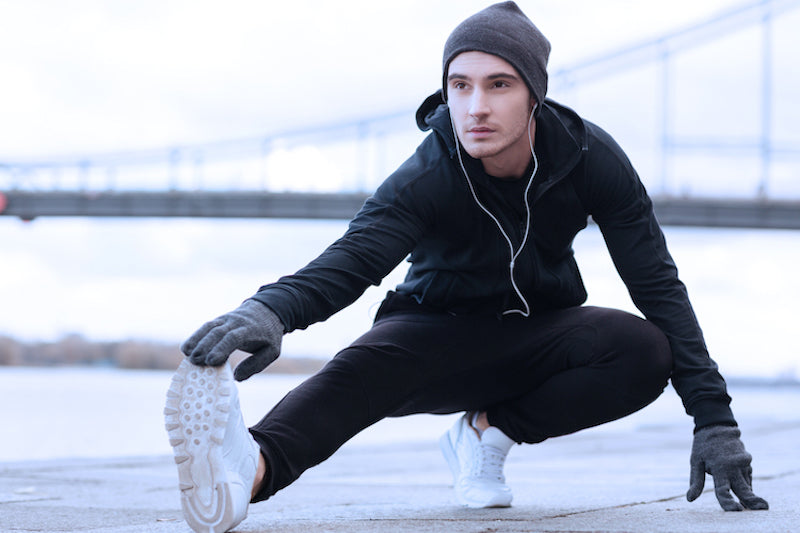 Man doing stretches outside, in front of a bridge in the distance