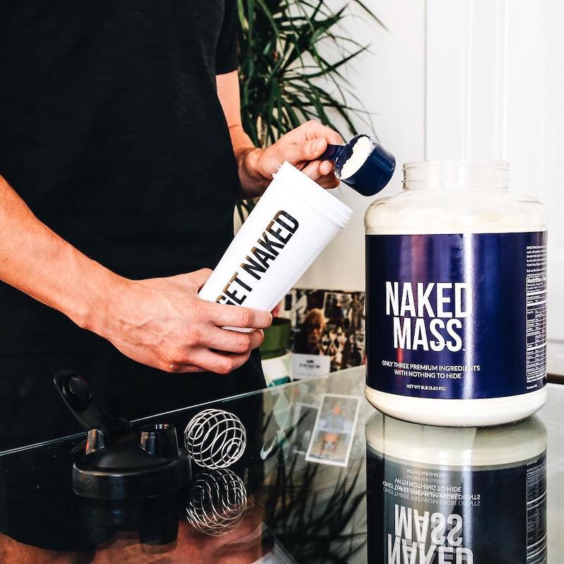 Naked Mass product image with a man putting a scoop of Naked Mass into a Naked Nutrition shaker bottle