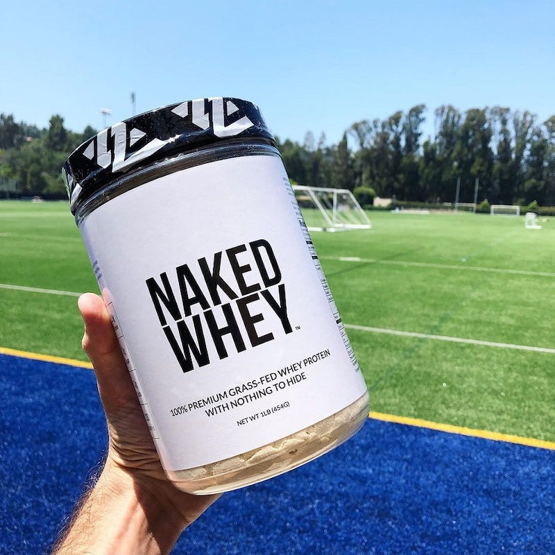 Naked Whey product image with the product is being held up in front of a sports field