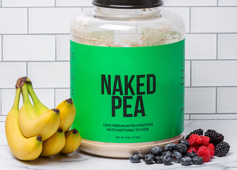 Naked Pea tub next to bananas and berries in front of a white wall