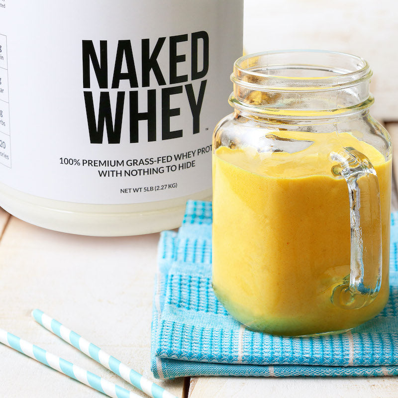 Tub of Unflavored Naked Whey behind a protein smoothie in a glass jar