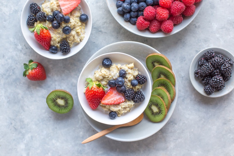 Bowls of oatmeal that are topped with blueberries, strawberries, and paired with slices of kiwi