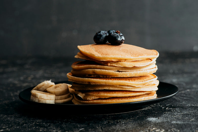 Stack of pancakes with blueberries on top and bananas on the side of the plate