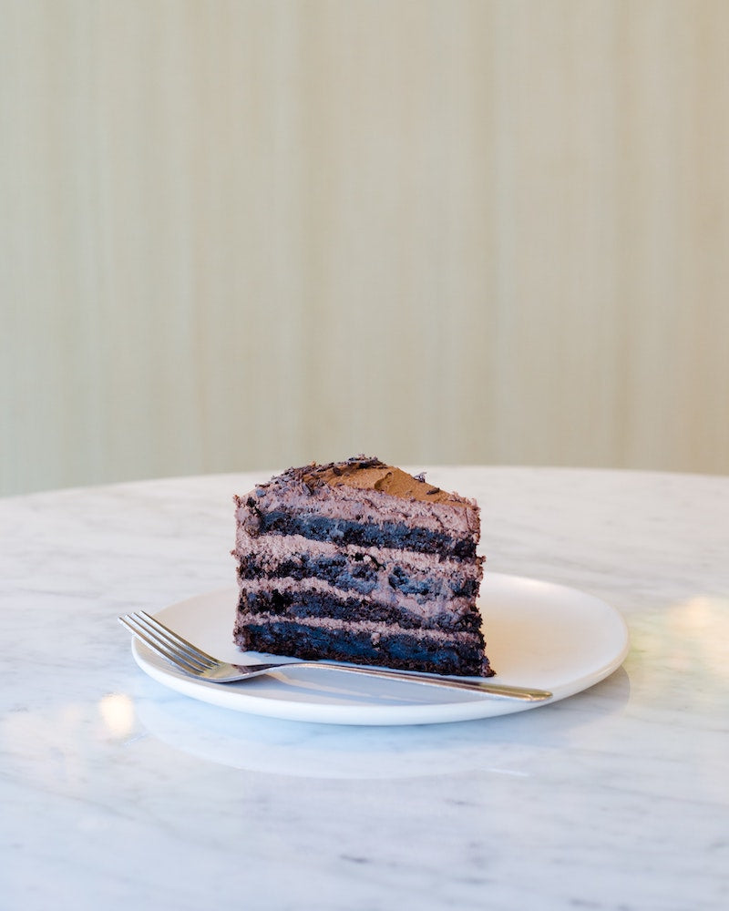 Slice of decadent protein powder chocolate cake on a plate in the middle of an empty table