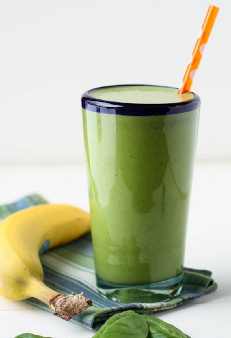 Green pea protein powder shake next to a banana and spinach leaves