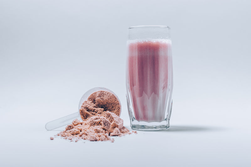 Image of a scoop of artificially colored strawberry protein powder next to a strawberry protein shake