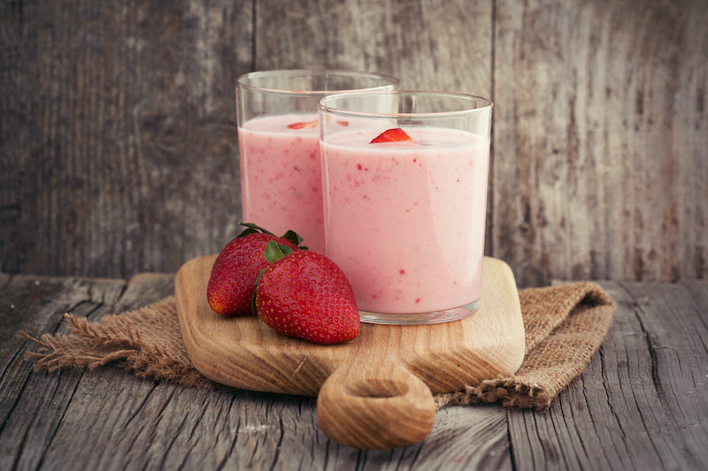 Collagen strawberry smoothies on a wooden board with two strawberries