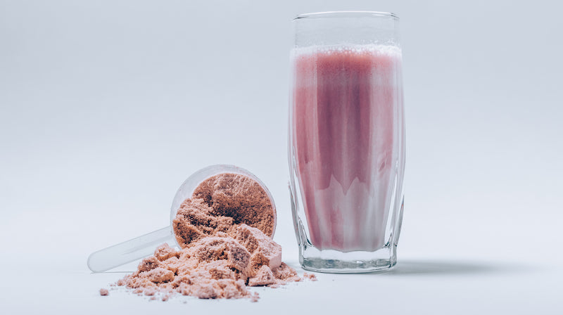 Scoop of dyed pink protein powder next to a pink protein shake