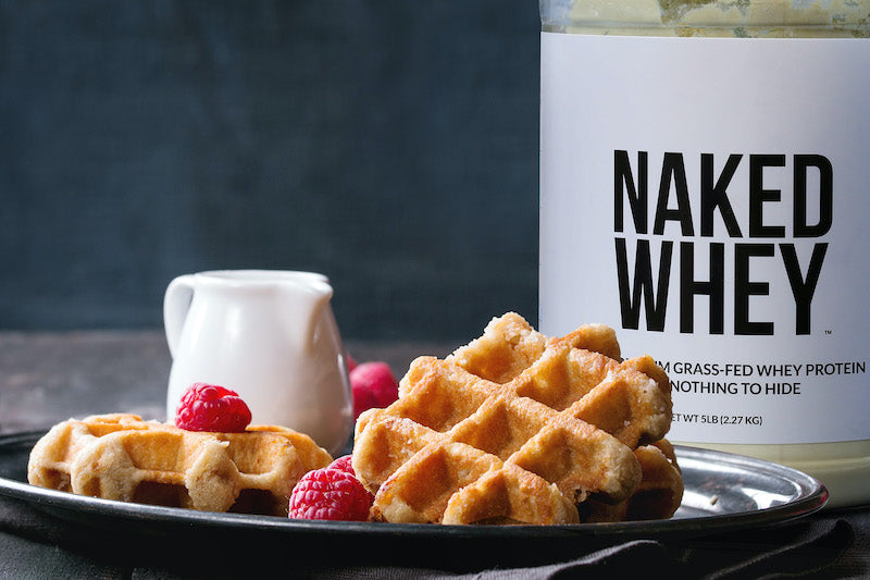 A tub of Naked Whey behind a plate of waffles and berries