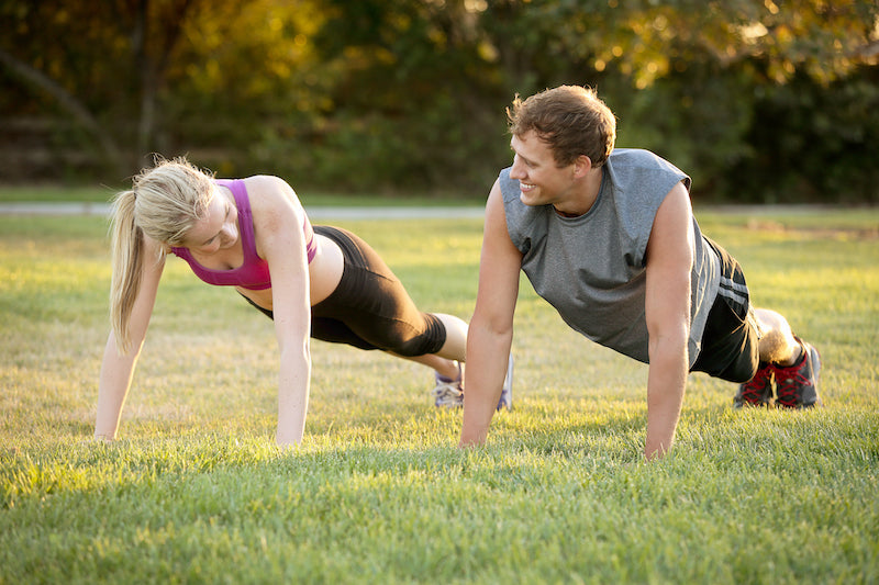 Man and woman doing push-ups outside in a field as workout partners