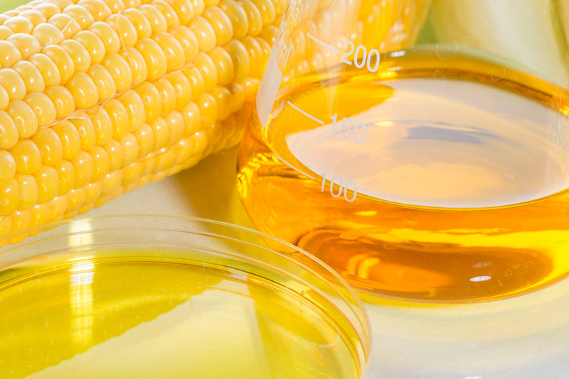 Glass container of corn syrup next to a cob of corn