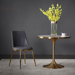 a vase of flowers on golden base tulip table with black chair