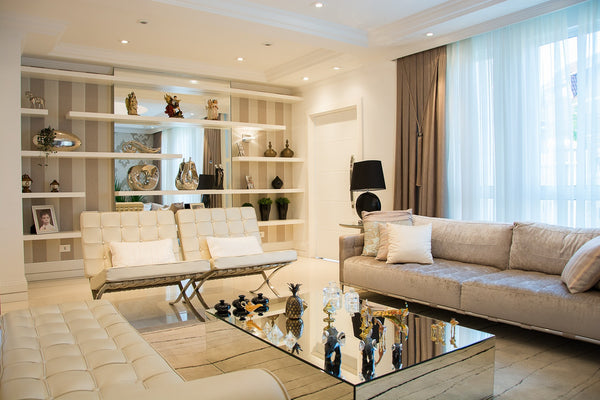 A mirror on the wall, many reflective ornaments on a table or shelf, a few pillows on a white sofa and a gray sofa with a gray rug underneath, very bright interior