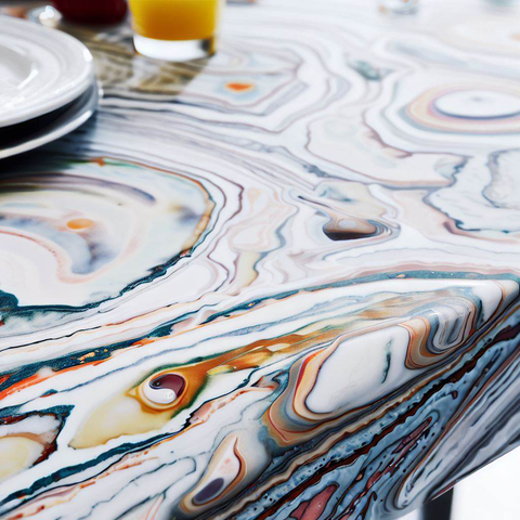 A close-up of a white marble dining table with a colorful pattern and some dishes