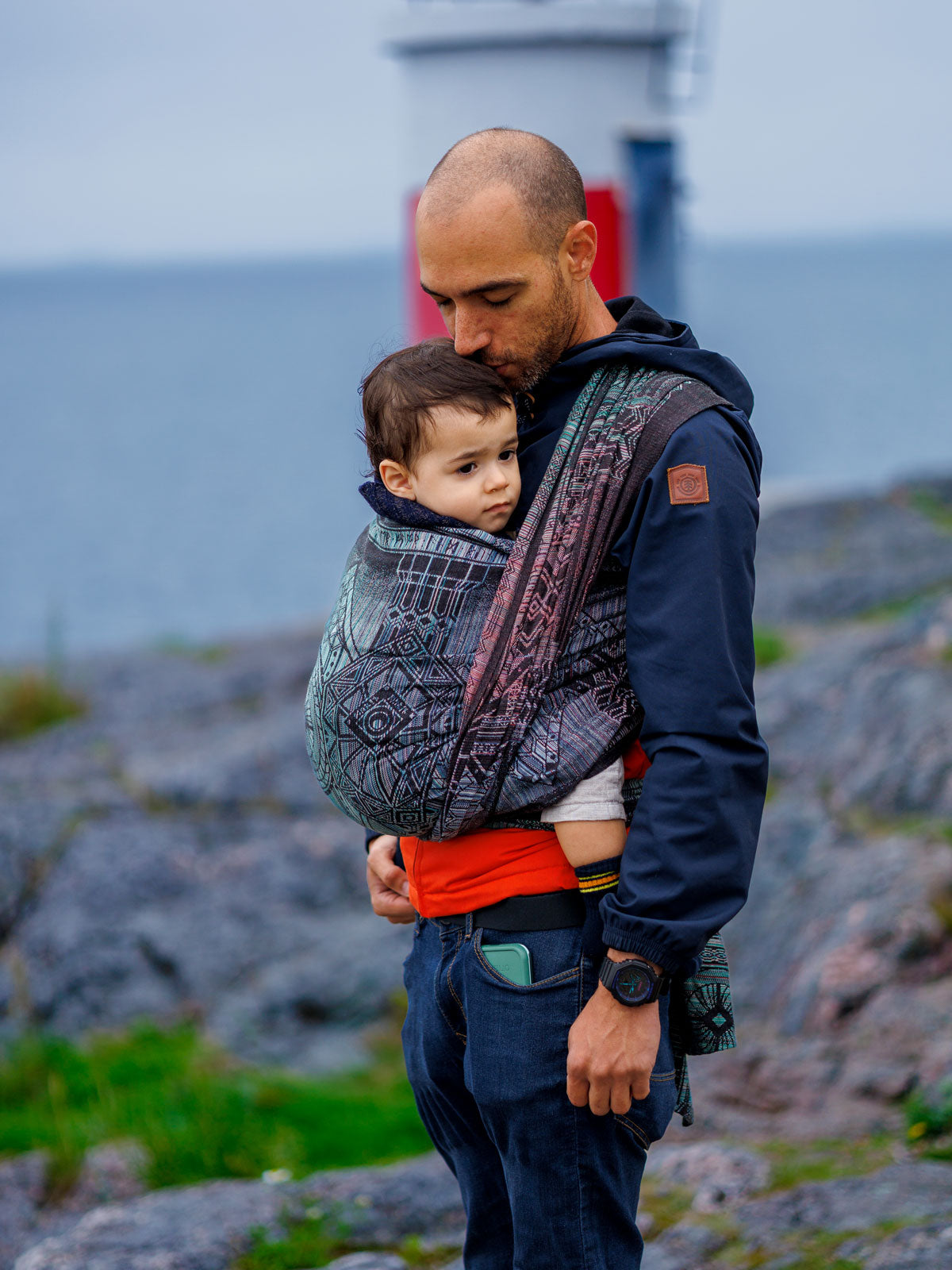 man baby carrying child in front of lighthouse