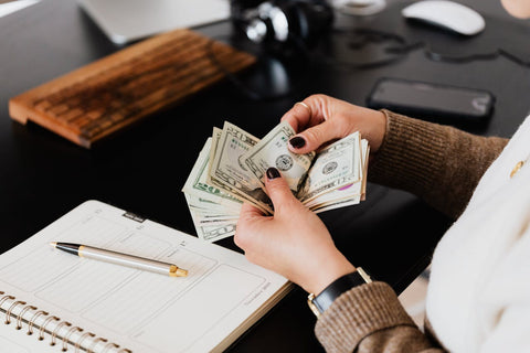 Person counting money next to a cellphone and notes