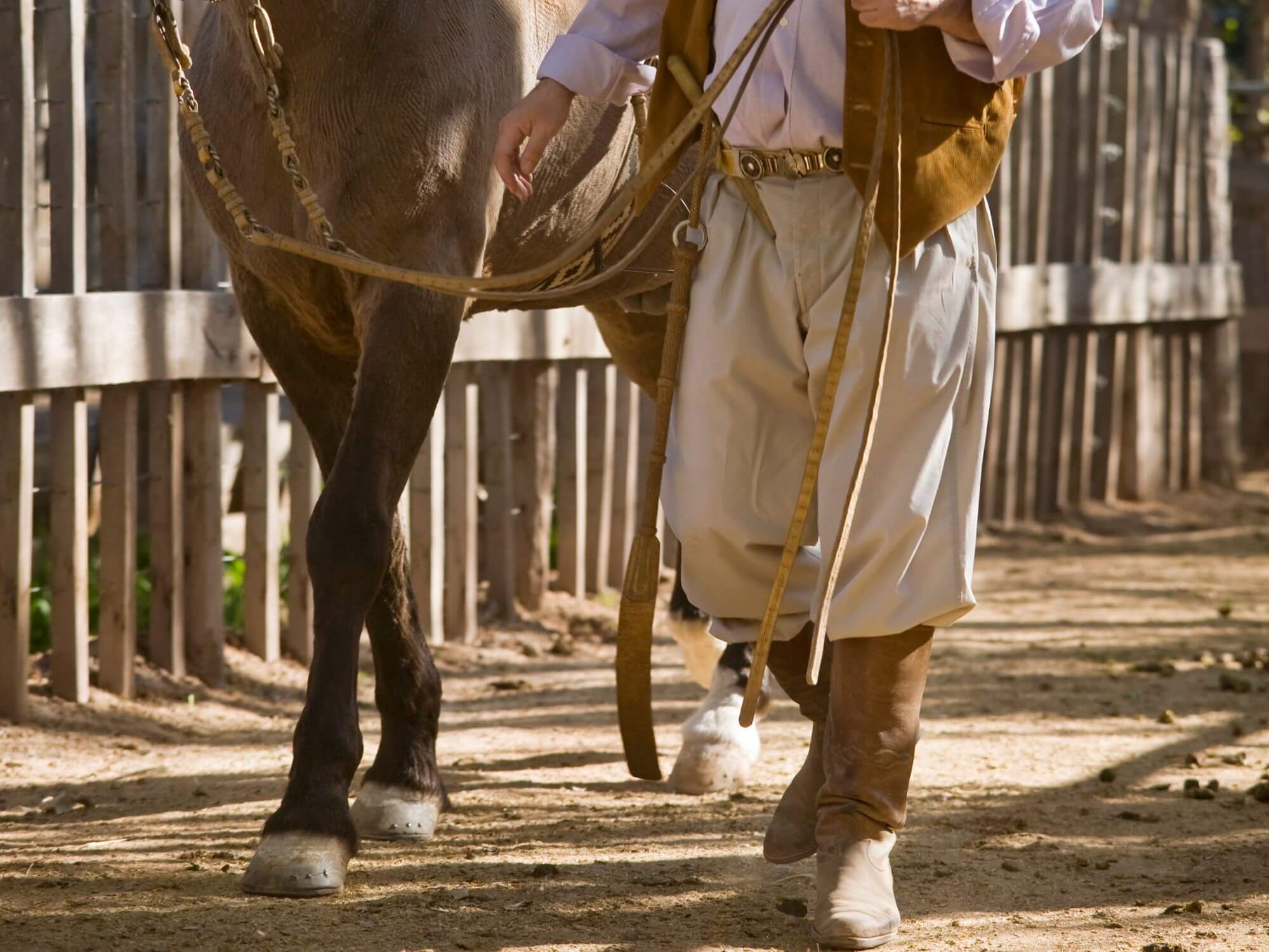 Homem segurando um cavalo e usando uma bombacha a tradicional calça gaúcha