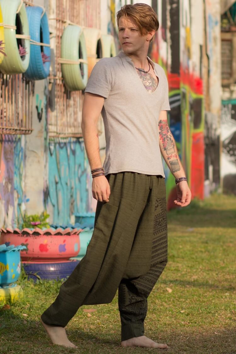 Homem loiro pé descalço com tatuagens usando a calça om verde em um gramado