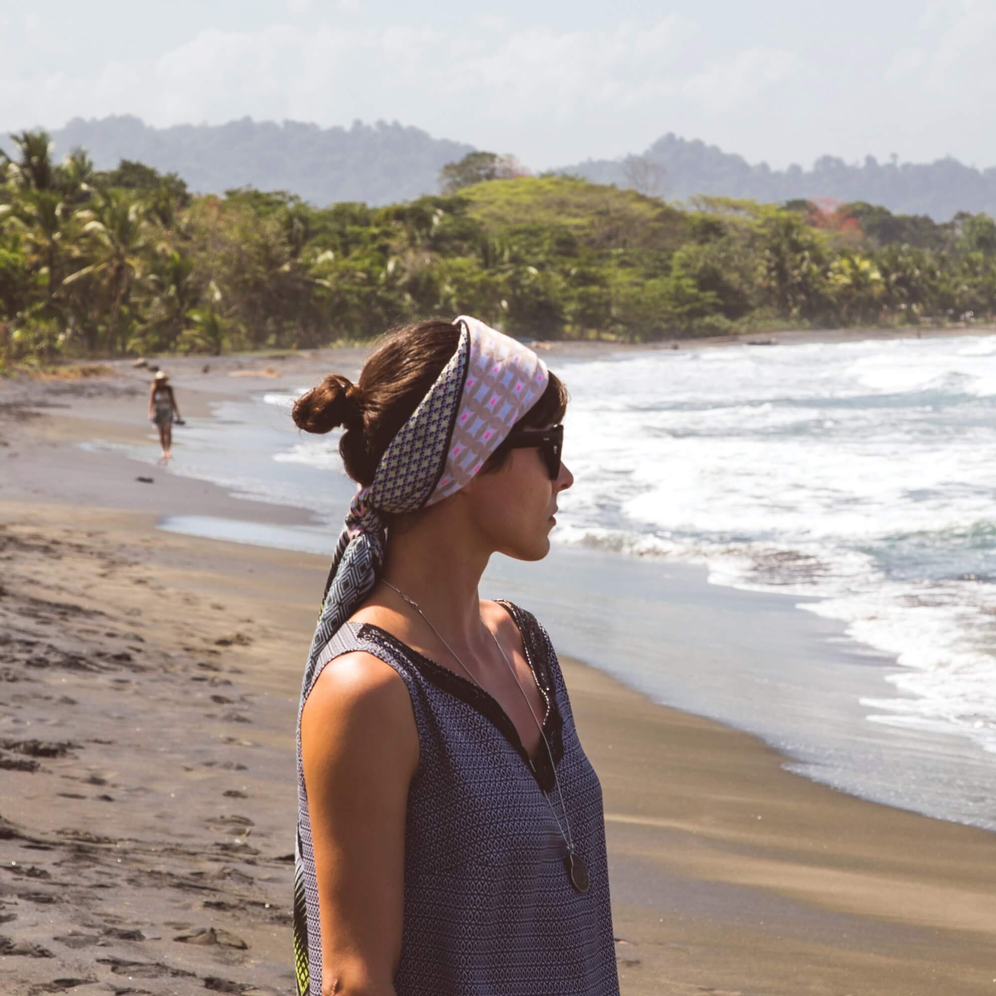 Mulher na praia com óculos de sol e um lenço estampado em volta da cabeça