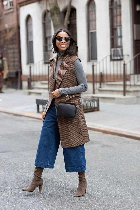 mulher atravessando a rua usando calça pantacourt, botas, blusa e colete