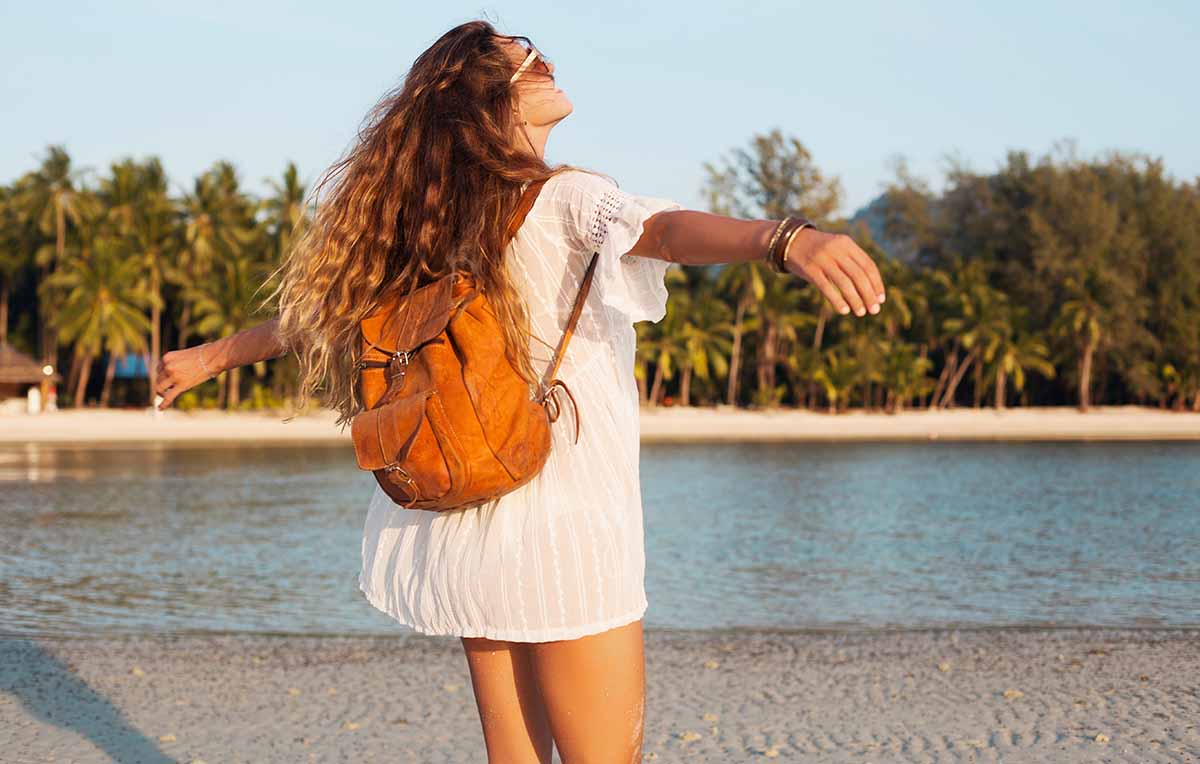 mulher na praia de braços abertos usando túnica como saída de praia