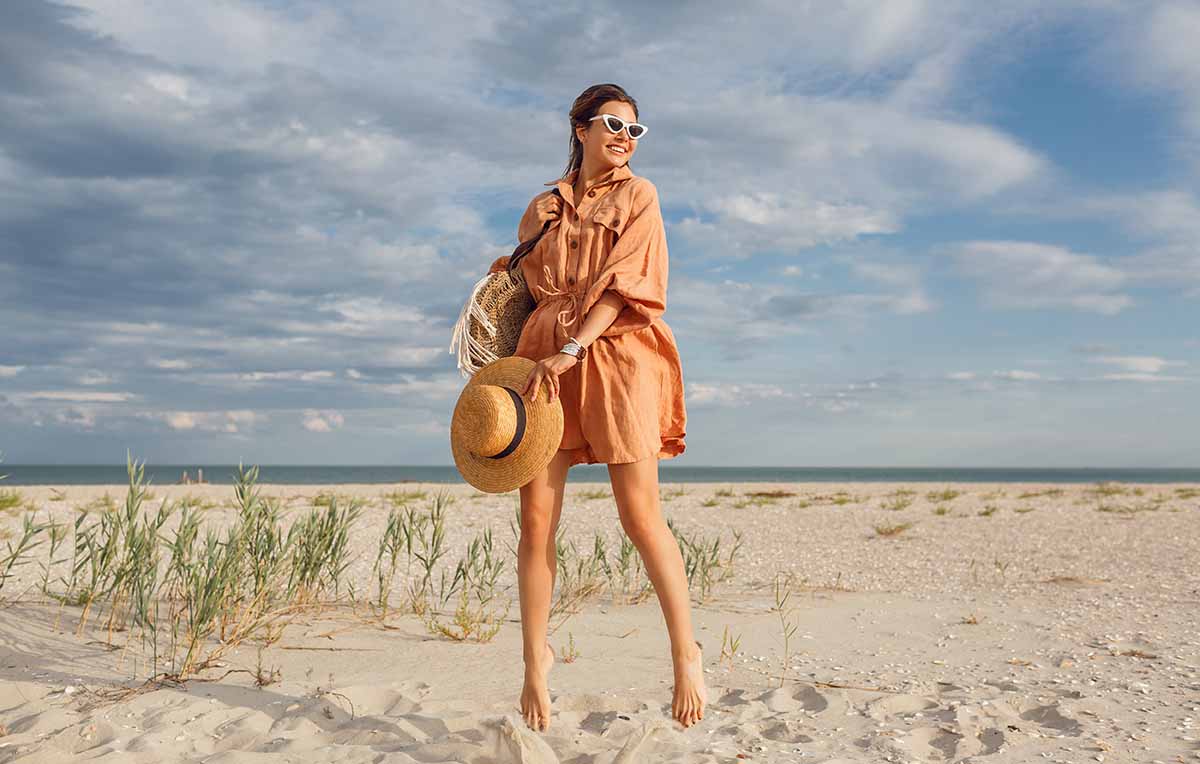 mulher pulando na areia da praia usando chemise como saída de praia