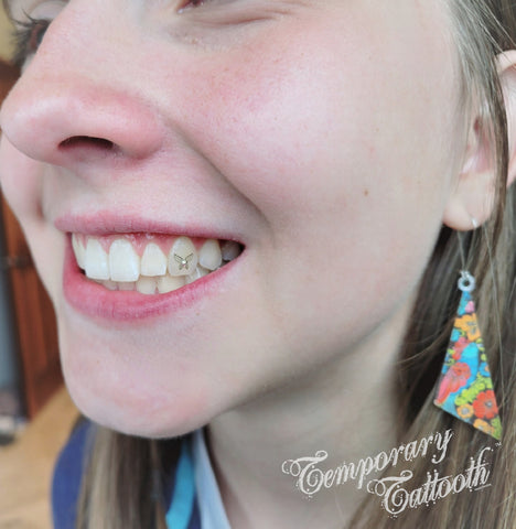 A photo of a girl with a butteryfly or toothfairy Temporary Tattooth with a tooth gem crystal in the center.