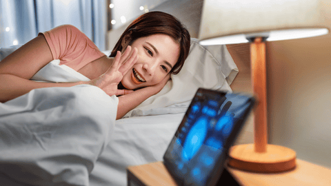 Women on bed speaking to tab for smart lighting